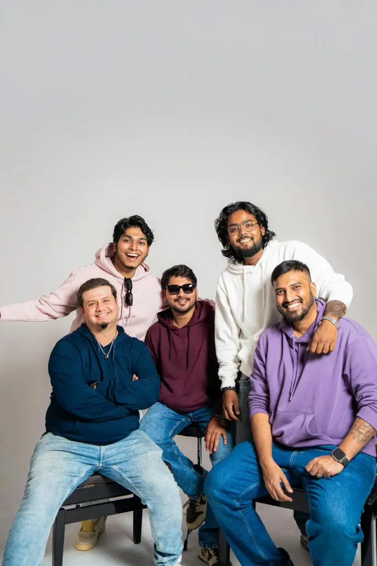 Five friends in casual hoodies smiling together in a studio setting.